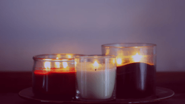 Três velas brancas acesas simbolizando as virtudes teologais - Fé, Esperança e Caridade - em um ambiente sereno e contemplativo